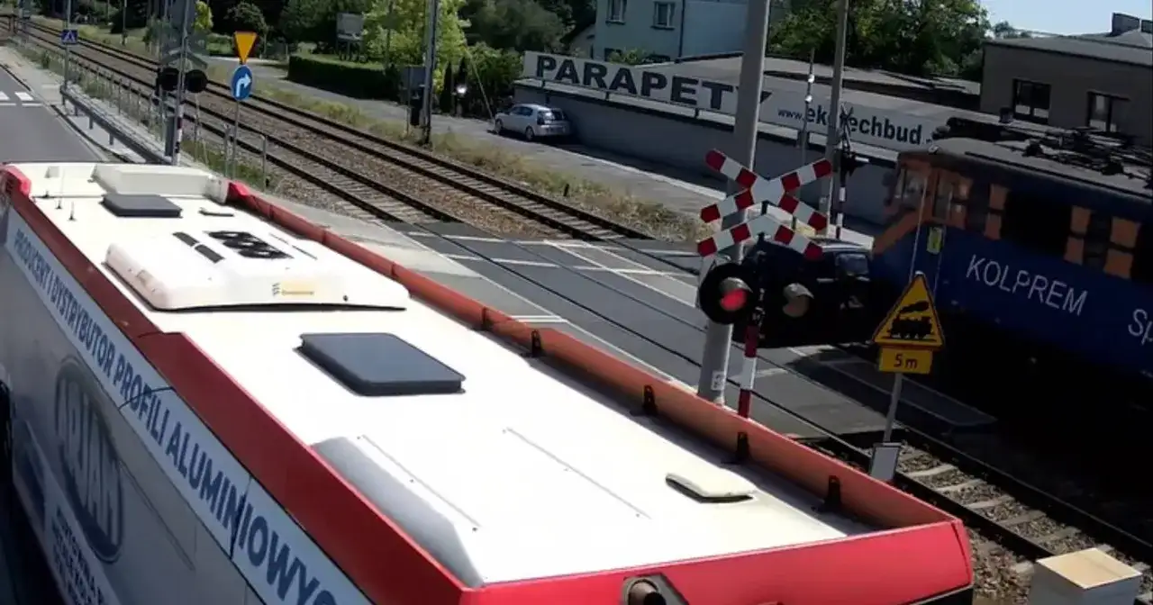 Autobus czeka na przejazd kolejowy w drodze do Częstochowy. Pociąg Kolprem mija przejazd.
