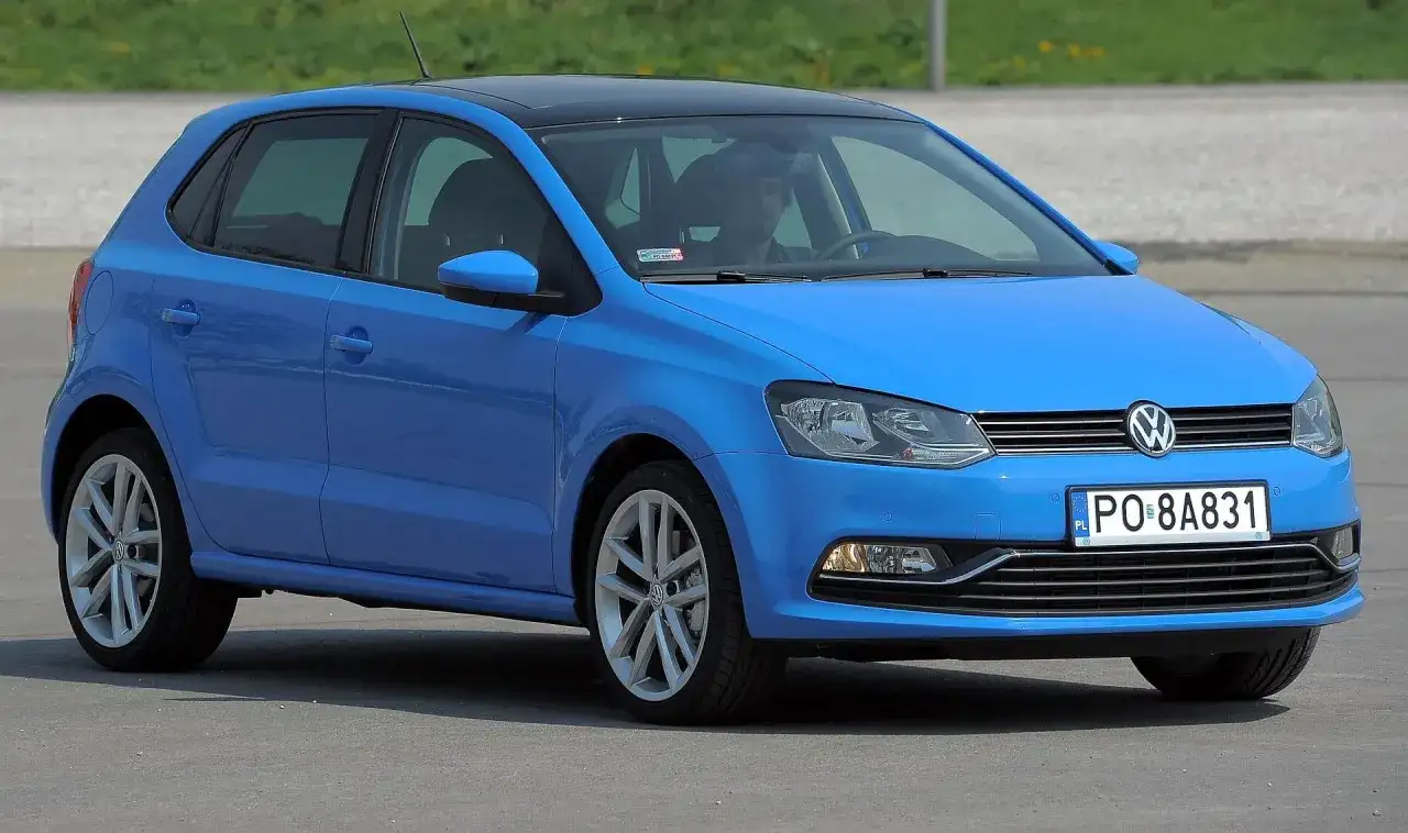 Niebieski VW Polo 2010 z czarnym dachem, zaparkowany na zewnątrz. Kierowca siedzi za kierownicą.
