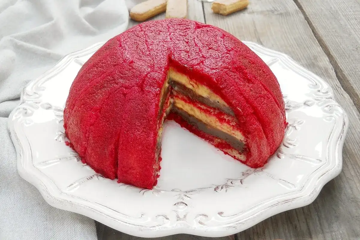 Zuppa inglese, un dessert a cupola con strati di crema e pan di Spagna, ricoperto da una glassa rossa vibrante.