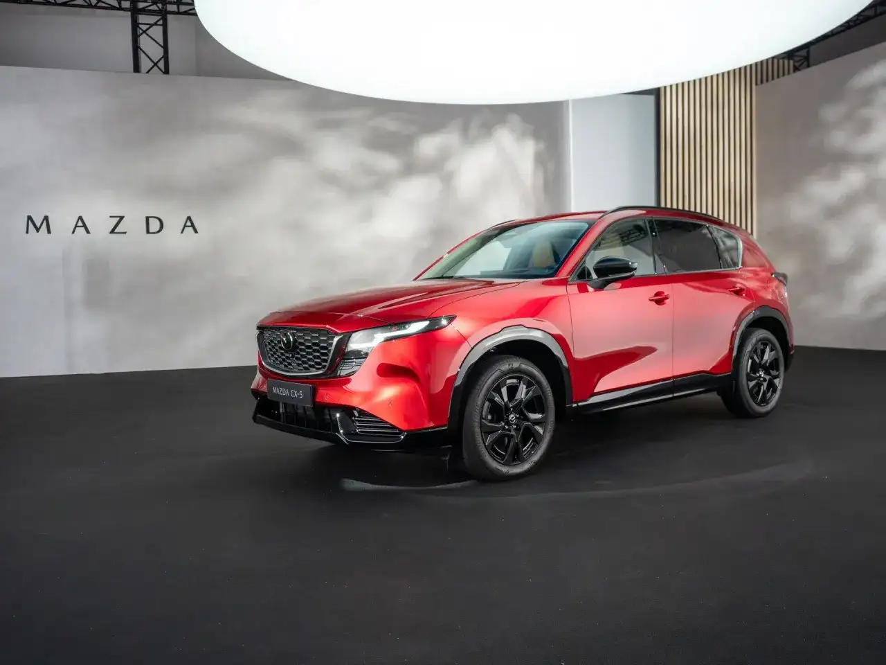 Lśniąca, czerwona Mazda CX-5 2026 prezentuje się na czarnej scenie.