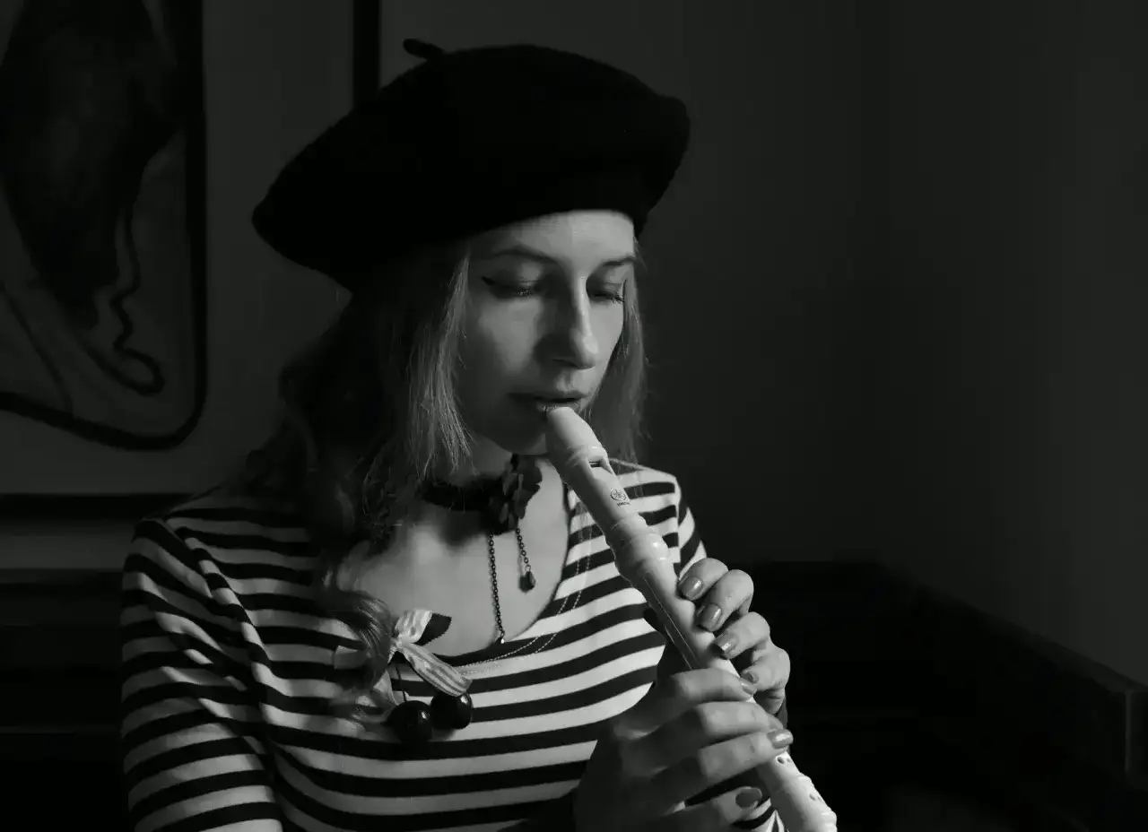 Kobieta w beretce gra na flecie. Pokazuje, jak się gra gamę na flecie, skupiona na melodii.