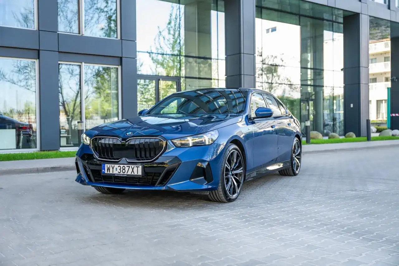 Eleganckie, granatowe BMW 540d z nowoczesnym designem, zaparkowane przed szklanym budynkiem.