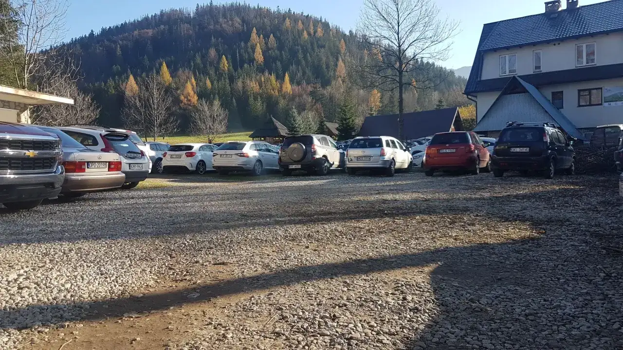 Parking w Kuźnicach, jesienny las na wzgórzu, rząd samochodów na żwirowym placu.