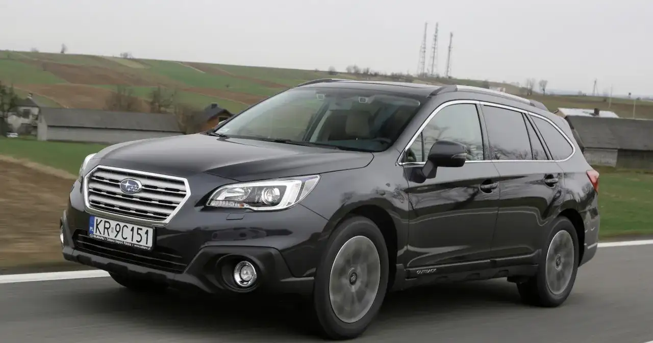 Ciemnoszary Subaru Outback 2025 na tle wiejskiego krajobrazu.