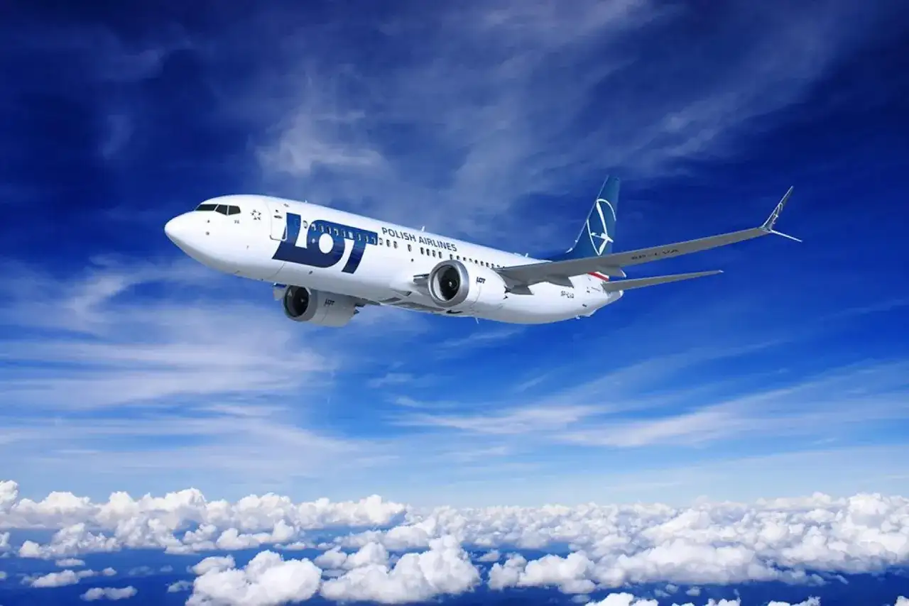 Samolot LOT Polish Airlines leci na tle błękitnego nieba z chmurami.