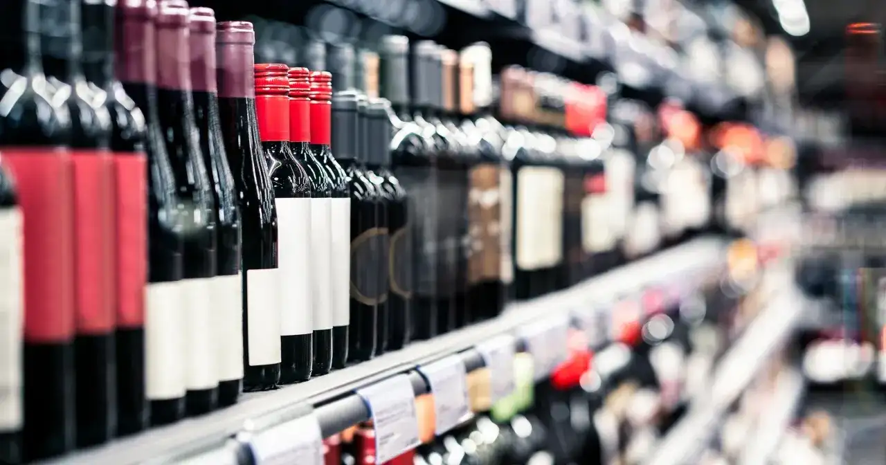 Rzędy butelek wina na półce sklepowej. Widać etykiety i ceny alkoholu, zachęcające do wyboru.