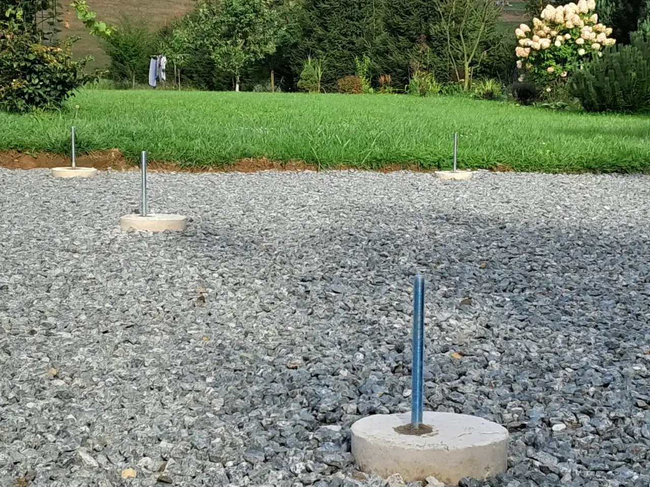 Gotowe fundamenty z betonu pod słupy wiaty, osadzone w żwirze.