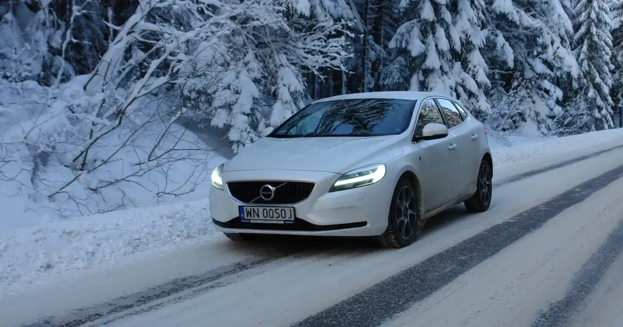 Białe Volvo V40 D3 pokonuje ośnieżoną drogę w lesie.
