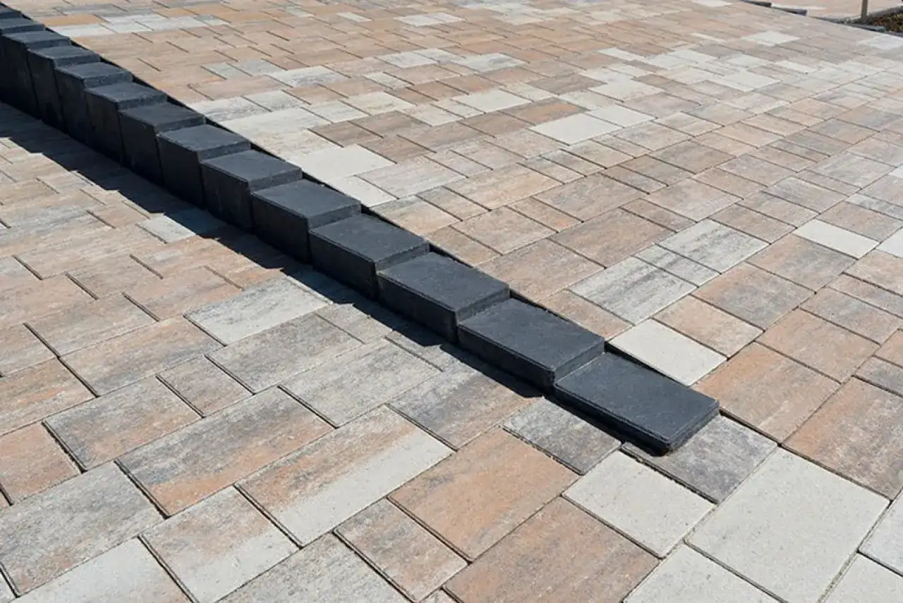 Nowa palisada z kostki brukowej tworzy elegancką linię na tarasie z kostki w odcieniach beżu i szarości.