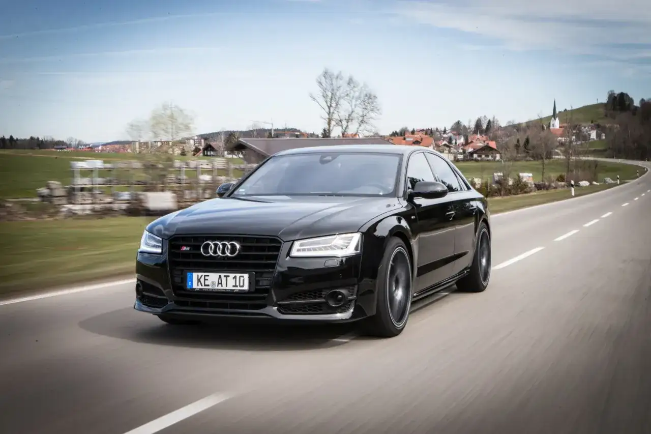 Czarny Audi RS8 pędzi po krętej drodze, mijając malowniczą wioskę.