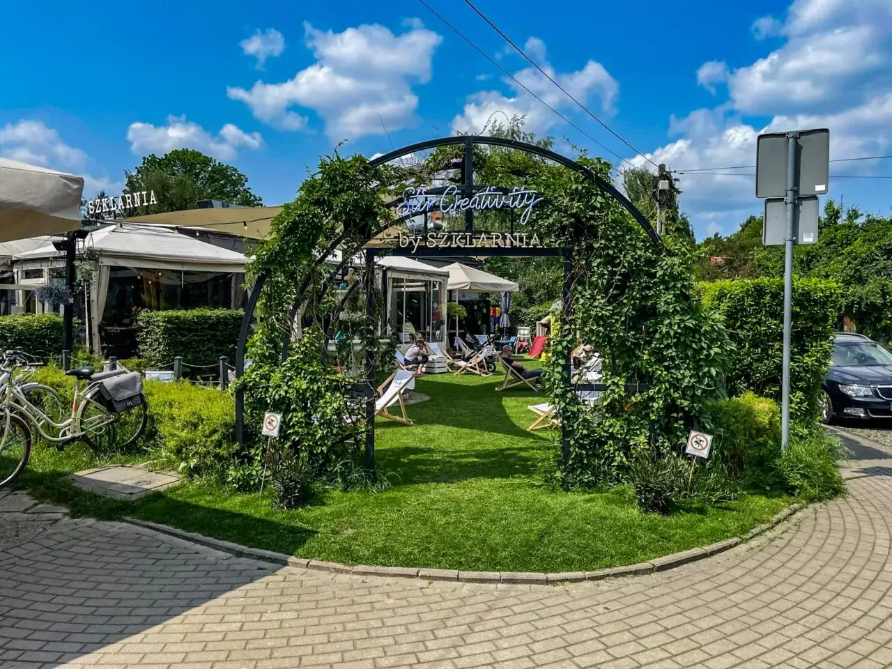 Letnie popołudnie w jednej z warszawskich restauracji z ogródkiem. Goście relaksują się na leżakach wśród zieleni.