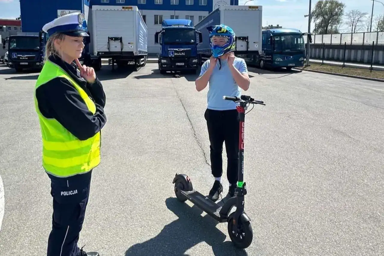 Policjantka sprawdza, czym można jeździć na kartę rowerową. Chłopiec zakłada kask na hulajnogę elektryczną.