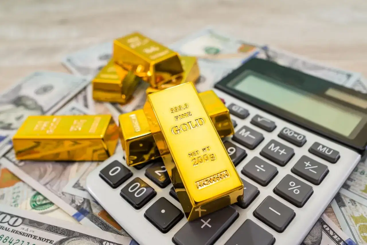 Sztabki złota na banknotach dolarowych i kalkulatorze symbolizują mądry gold investment.
