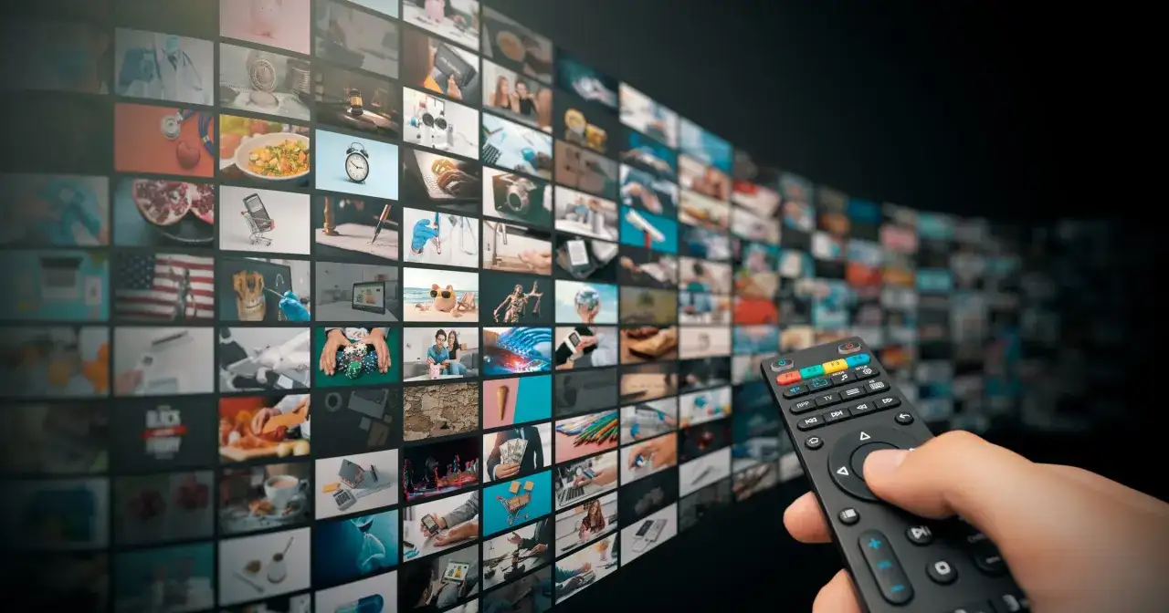 Dłoń trzyma pilota, wybierając treści z zakrzywionego ekranu pełnego miniatur, jak w interaktywnym menu HbbTV.
