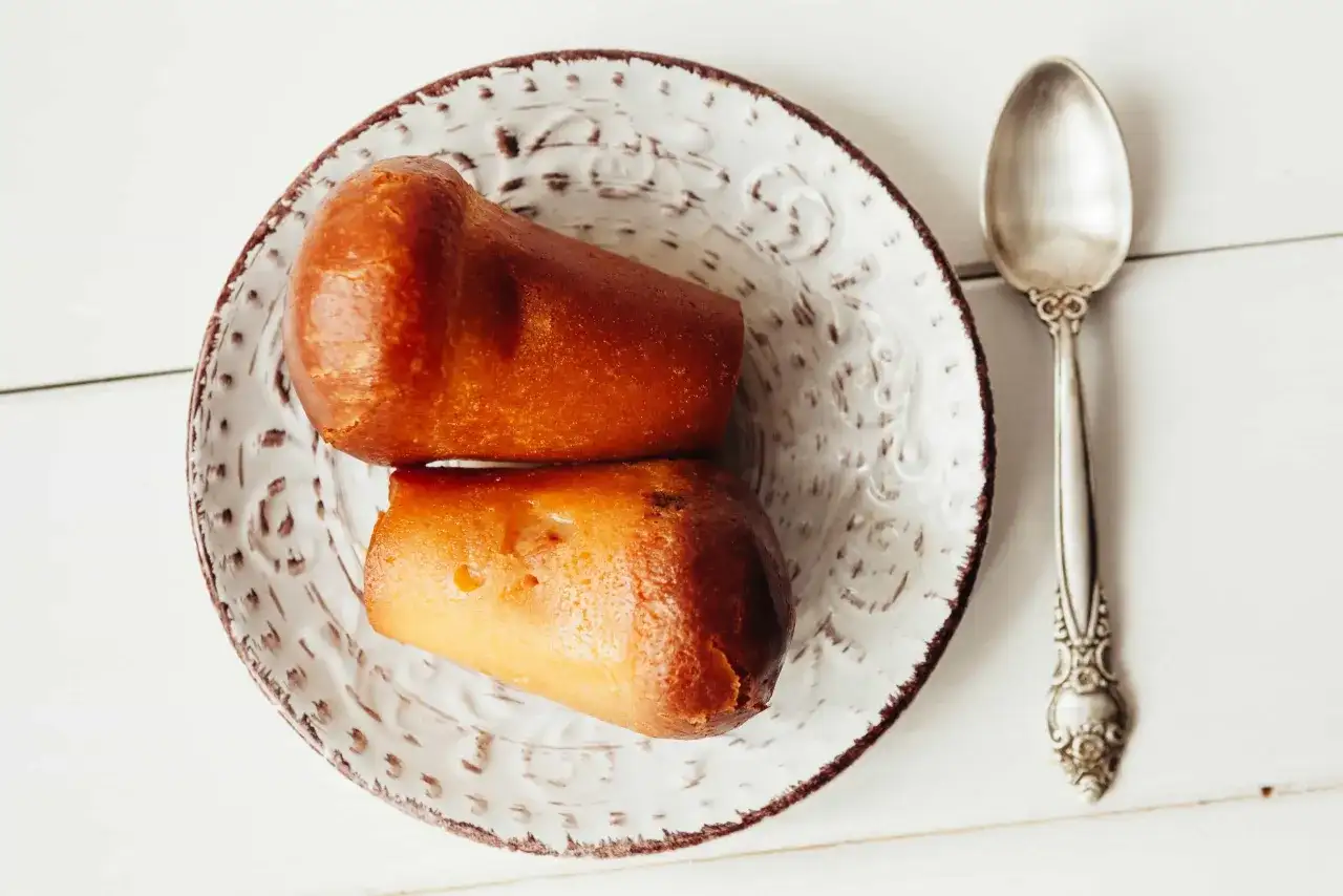 Deux baba au rhum dorés sur une assiette décorée, prêts à être dégustés avec une cuillère argentée.