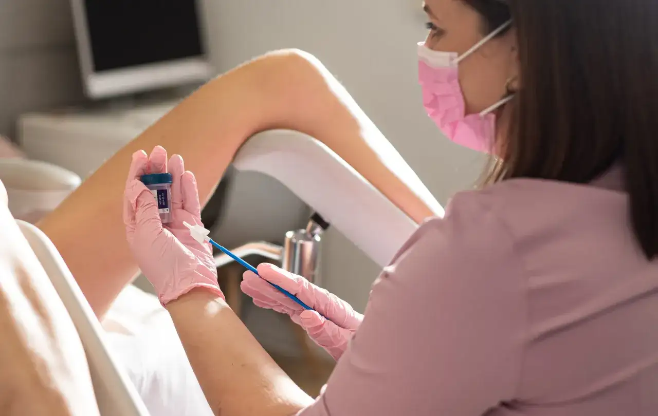 Lekarka w różowej masce i rękawiczkach przygotowuje się do pobrania wymazu. Czy cytologia boli? To badanie jest zazwyczaj bezbolesne.