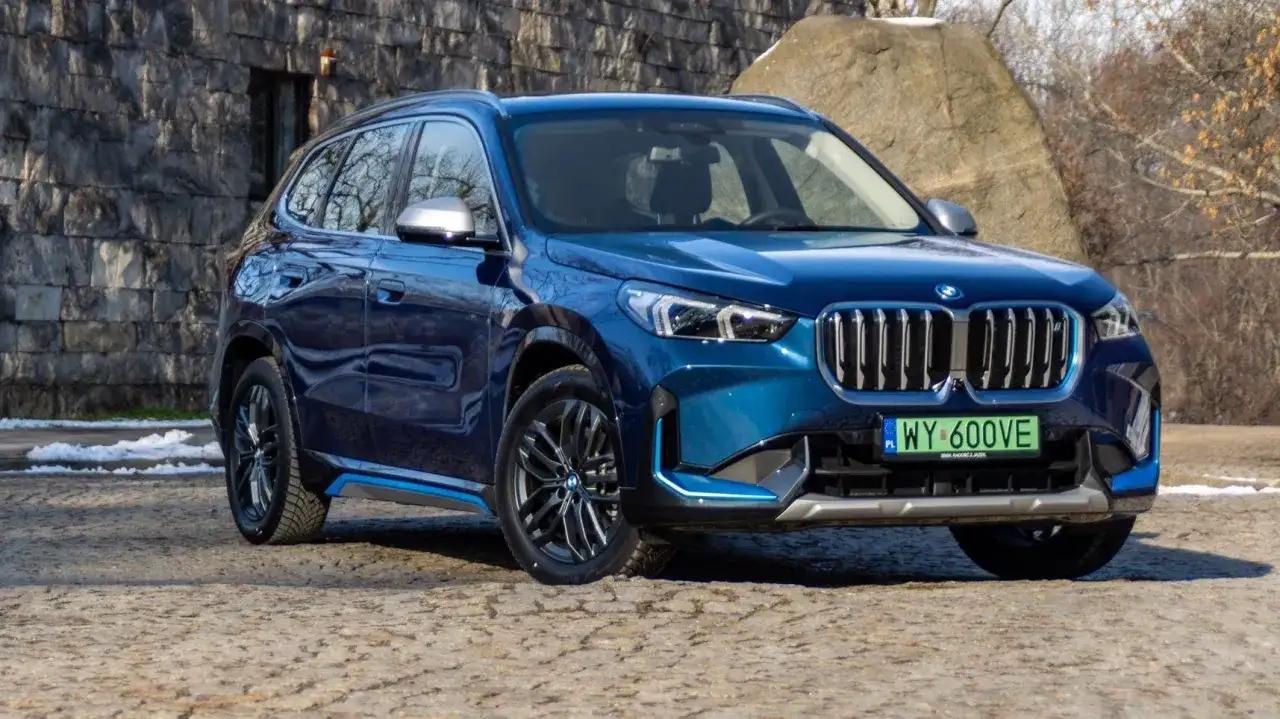Błękitny BMW X1 elektryk z niebieskimi akcentami stoi na kamienistej drodze.