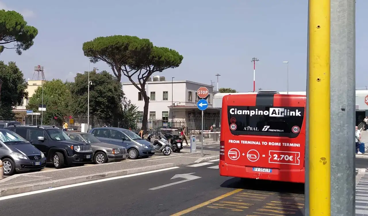 Czerwony autobus Ciampino Airlink, jadący do Rome Termini, stoi na parkingu obok innych samochodów.