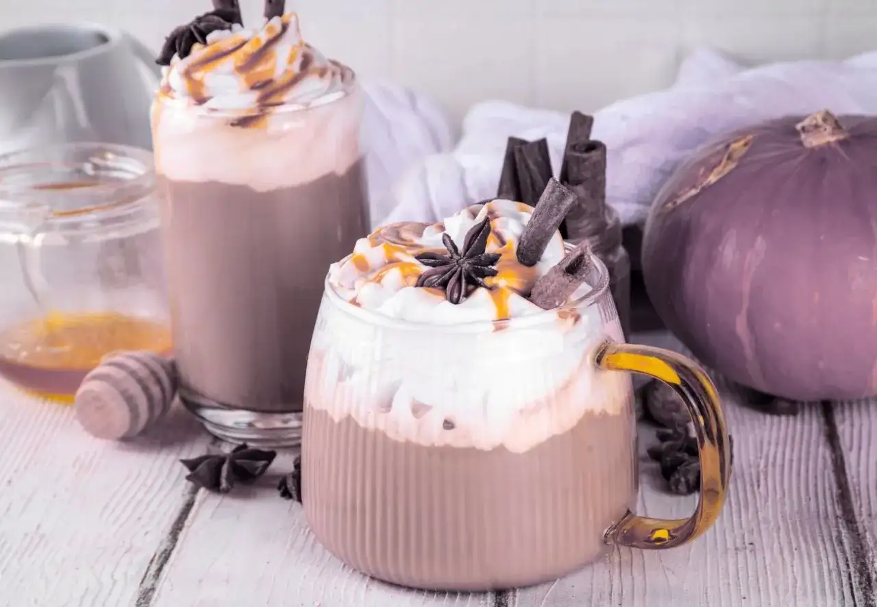Dwie pyszne pumpkin spice latte kawa z bitą śmietaną, karmelem i cynamonem. Obok dynia i miód.