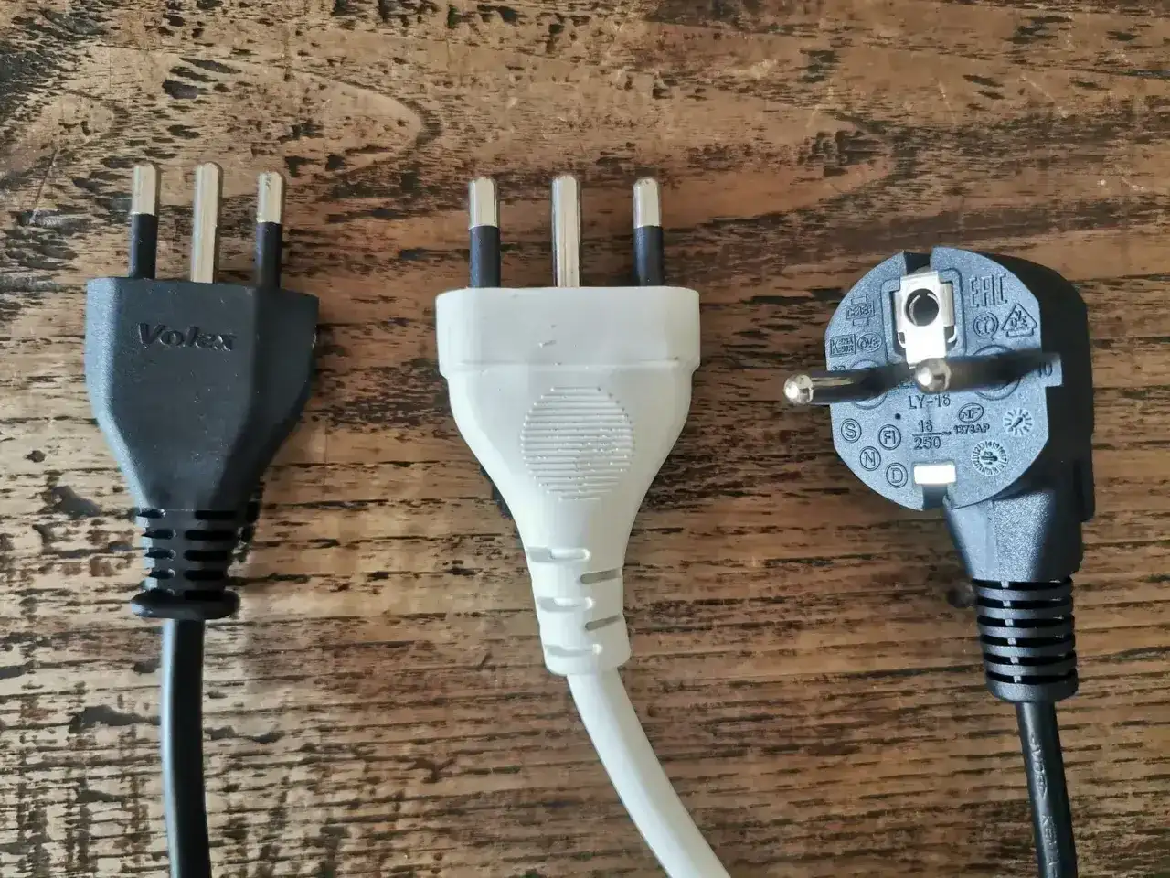 Trzy wtyczki elektryczne, w tym dwie z trzema bolcami, typowe dla gniazdek we Włoszech, leżą na drewnianym blacie.