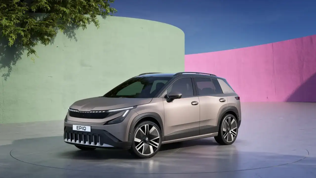 Nowy, elektryczny SUV Škoda Enyaq, z nowoczesnym designem i napisem Enyaq na grillu, prezentuje się na tle kolorowych ścian.