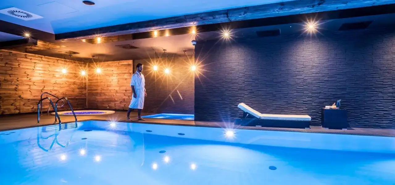 Mężczyzna w szlafroku spaceruje po luksusowej strefie dla dorosłych z basenem i jacuzzi.
