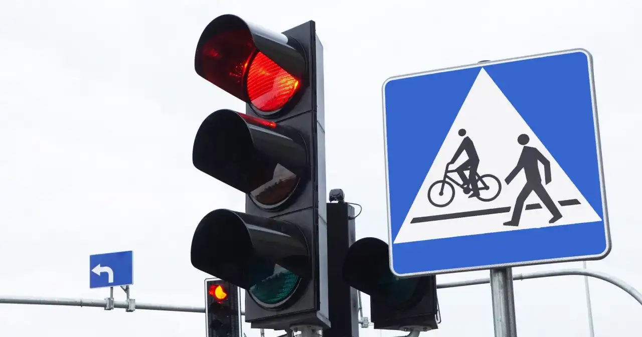 Sygnalizacja świetlna pokazuje czerwone światło, a obok znak informuje o przejściu dla pieszych i rowerzystów. Nie ryzykuj przejazdu na czerwonym świetle!