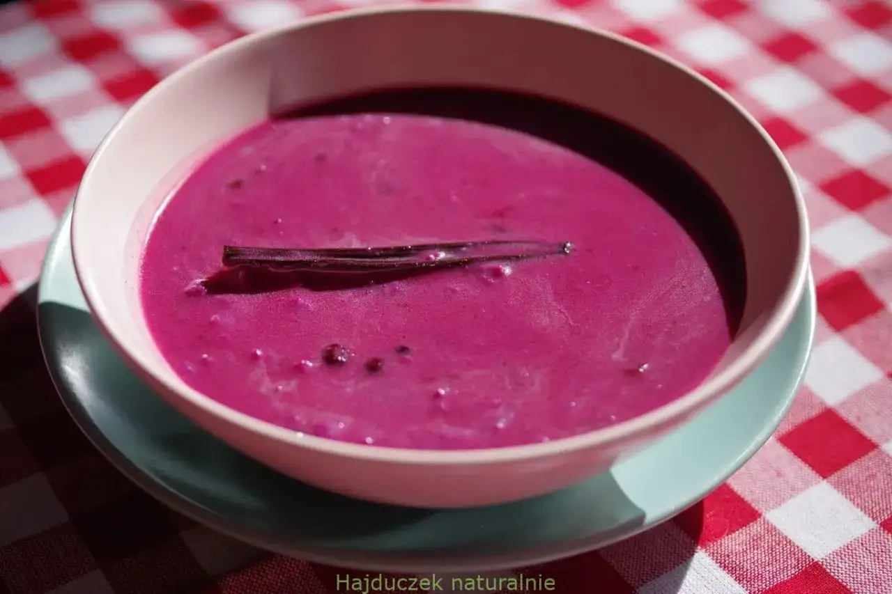 Aksamitna zupa jagodowa z laską wanilii, podana w miseczce na kraciastym obrusie.