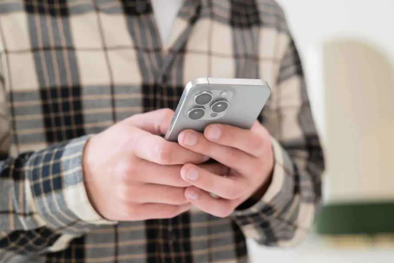 Osoba w kratę trzyma smartfon, szukając informacji, jak odzyskać usunięte wiadomości SMS.