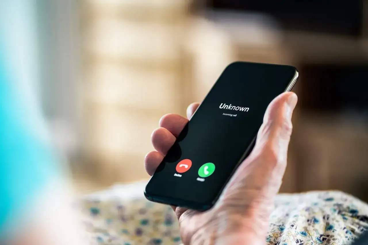 Dłoń trzyma smartfon z ekranem pokazującym "Unknown" i przyciski odbierania/odrzucania. Zastanawiasz się, kto dzwonił, numer jest nieznany.
