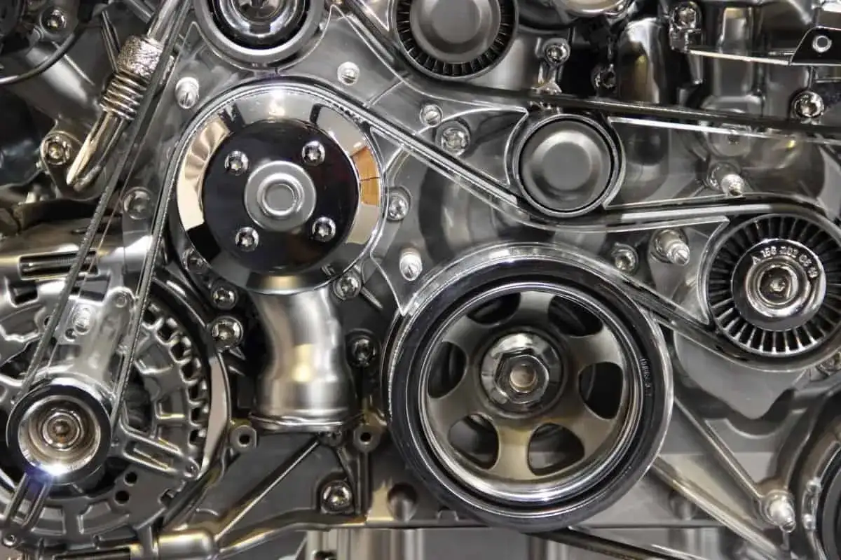 Détail d'un moteur chromé, avec la courroie de distribution tendue entre plusieurs poulies.