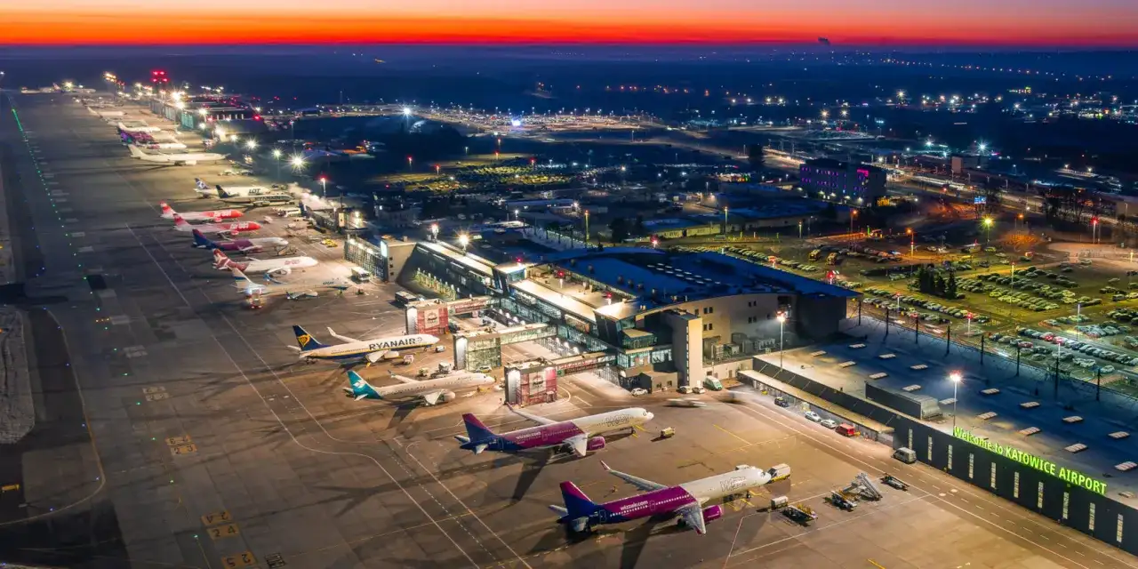 Lotnisko Katowice-Pyrzowice nocą, z samolotami na płycie i oświetlonym terminalem. Rozkład lotów pyrzowice jest dynamiczny.