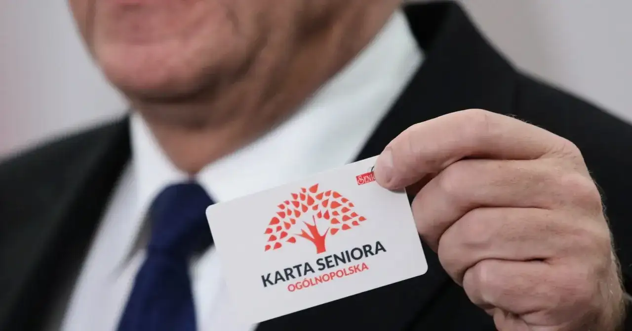 Mężczyzna prezentuje kartę seniora z czerwonym drzewem. To ogólnopolska karta uprawniająca do zniżek.