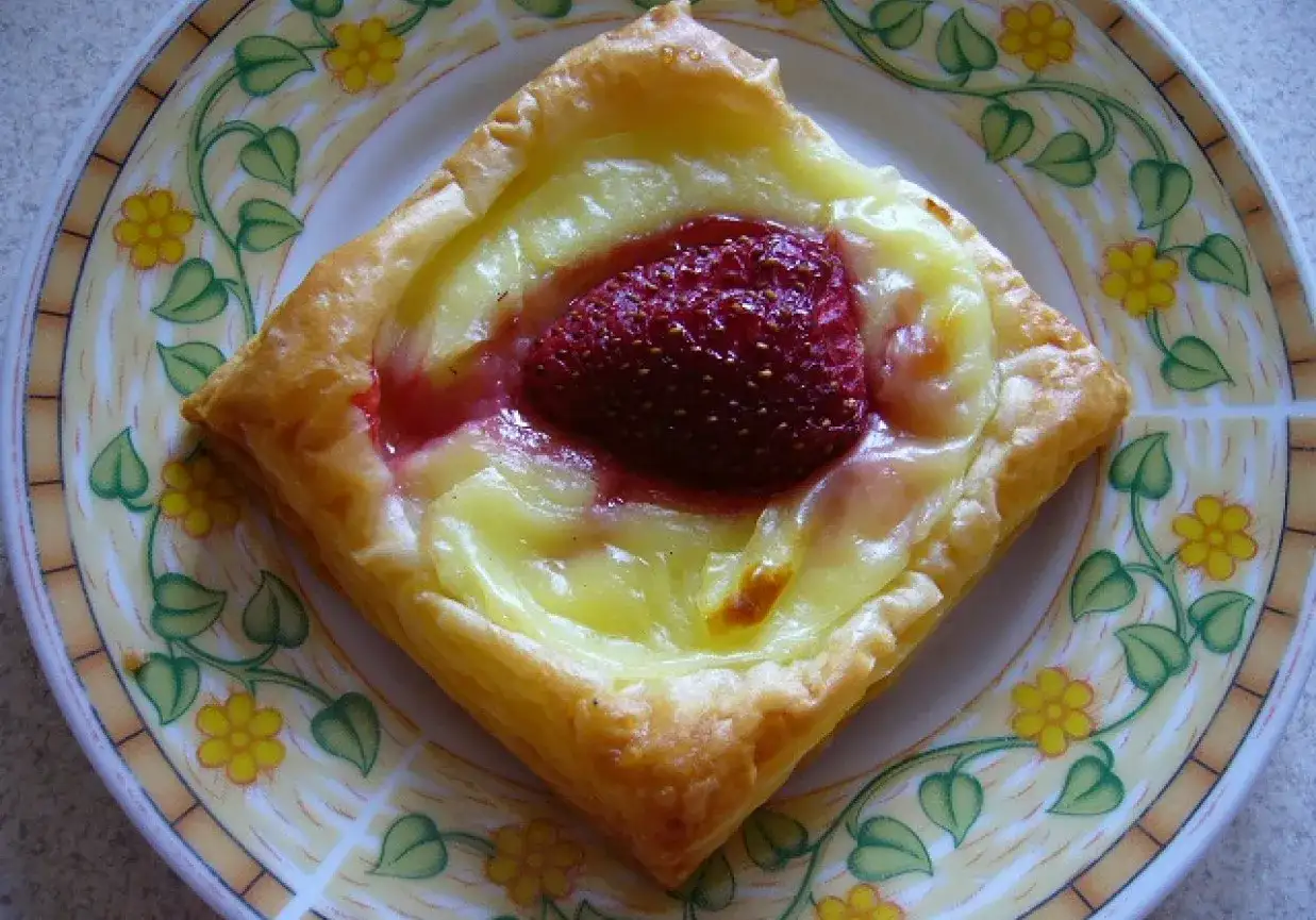 Pyszne ciasto francuskie z budyniem i truskawką na talerzu z kwiatowym wzorem.