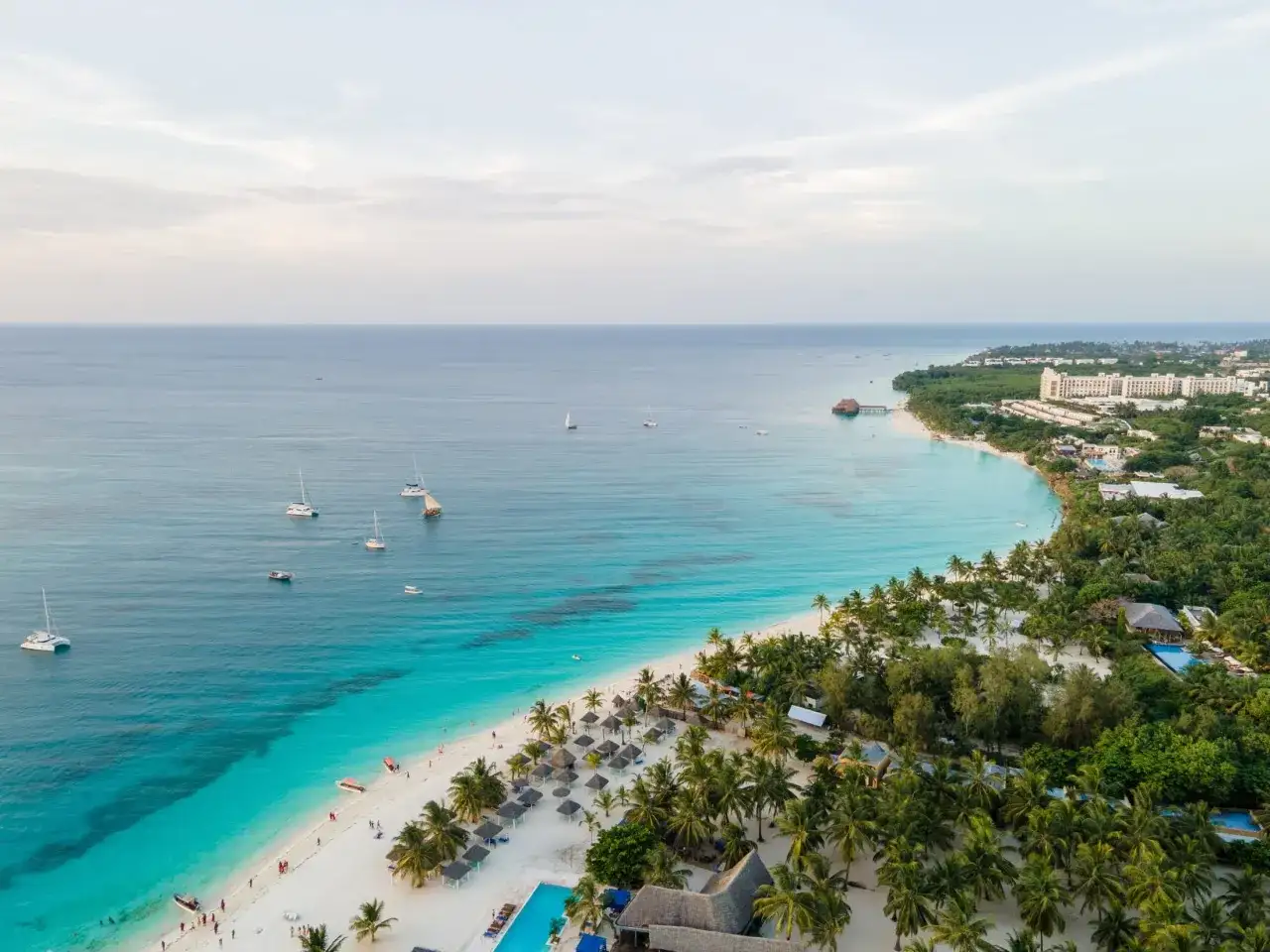 Rajska plaża na Zanzibarze z turkusową wodą, palmami i łodziami. Sprawdź aktualne zanzibar ceny, by zaplanować wymarzone wakacje.