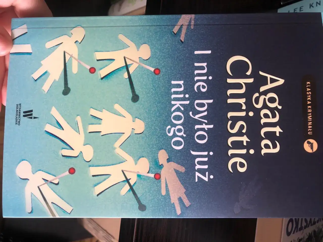 Okładka książki Agaty Christie "I nie było już nikogo". Papierowe ludziki z czerwonymi kropkami, jakby trafione.