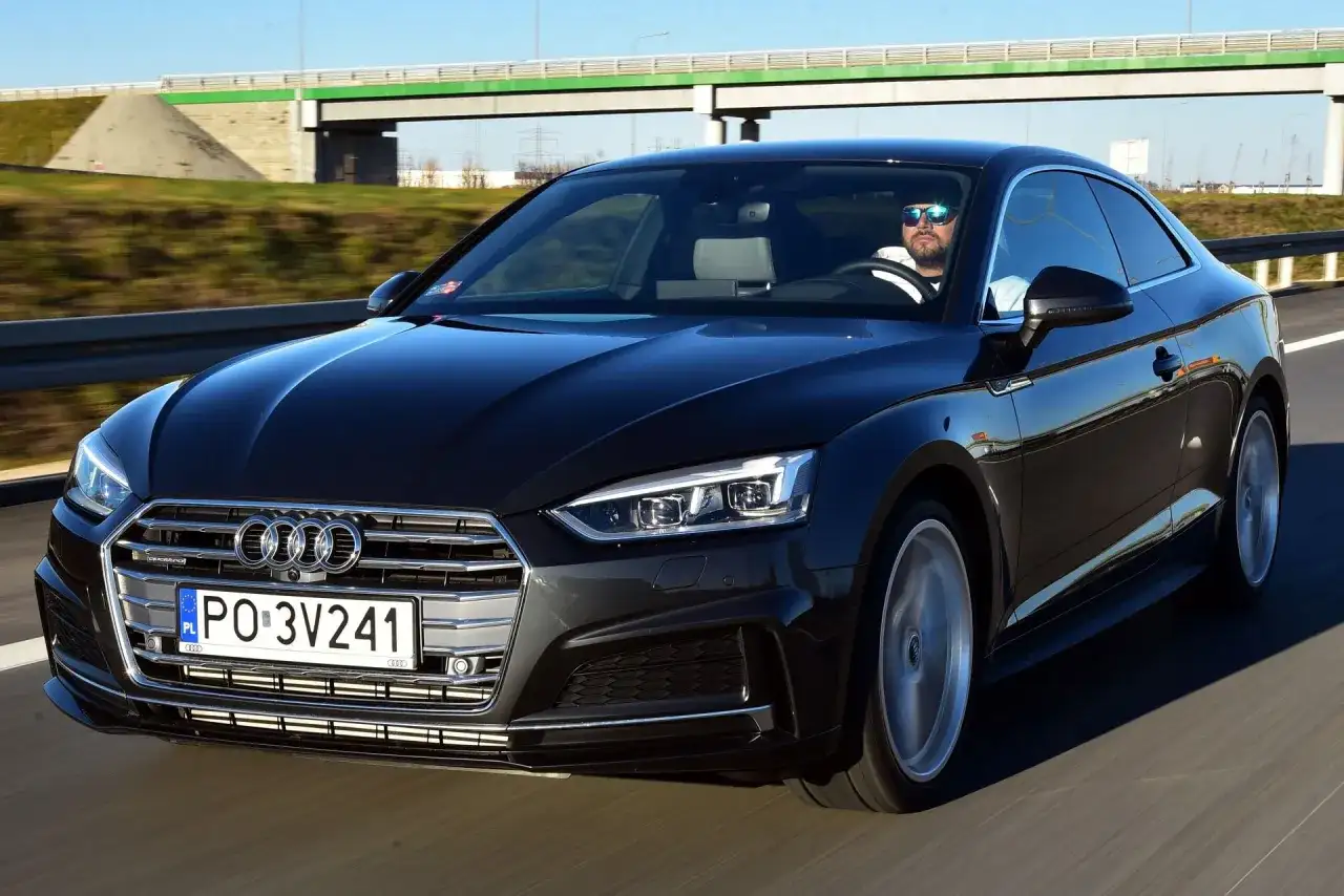 Czarny Audi A5 F5 z kierowcą w okularach przeciwsłonecznych jedzie autostradą.