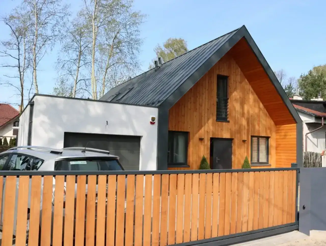 Nowoczesny dom z murowaną częścią i garażem, do którego przylega dobudówka drewniana.