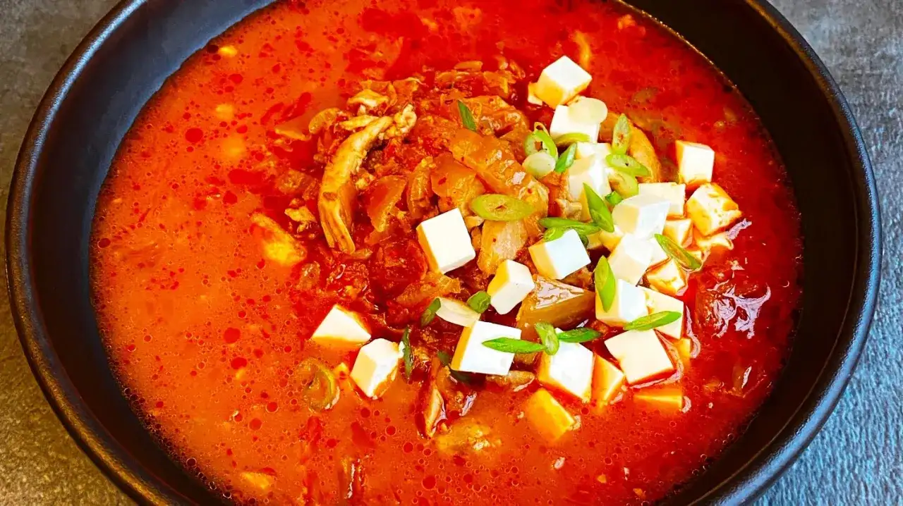 Pikantna zupa kimchi z kurczakiem i kostkami tofu, udekorowana szczypiorkiem.