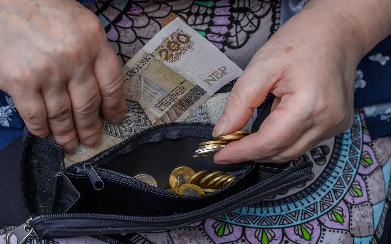 Dłonie chowają banknot 200 zł i monety do portmonetki. Nowe zasady emerytury po mężu to dla wielu nadzieja na stabilność finansową.