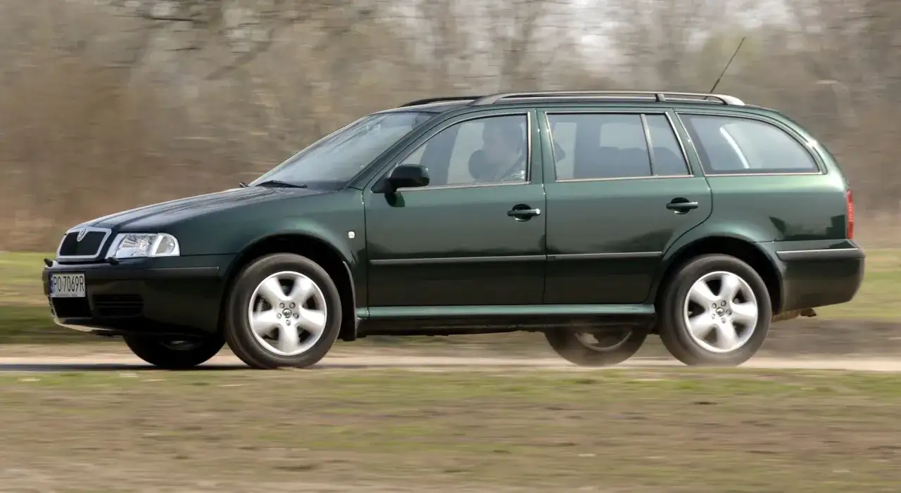 Zielona Skoda Octavia 2010 kombi jedzie po polnej drodze, unosząc kurz.