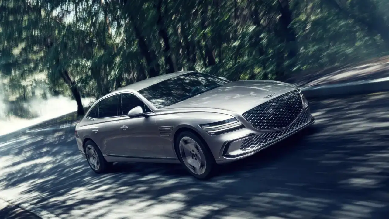 Silver Genesis G80 Sverige glider genom en skogsväg, skuggor dansar över bilen.