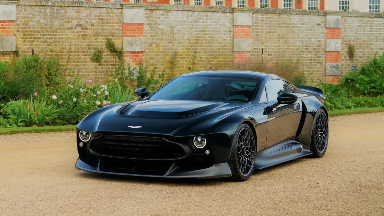 Elegancki, czarny Aston Martin Victor prezentuje się majestatycznie na tle zabytkowego dworu i bujnej zieleni.