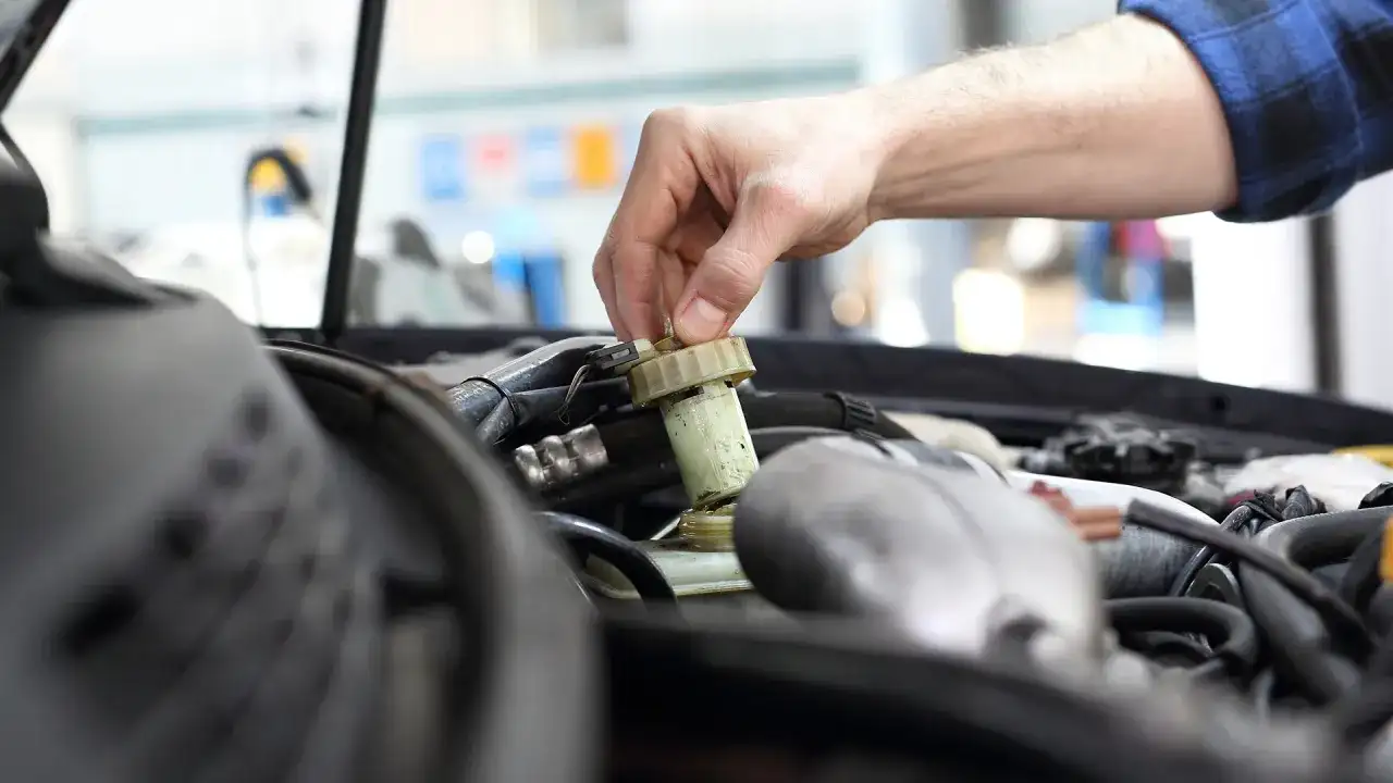 Ręka mechanika odkręca zakrętkę zbiorniczka płynu hamulcowego. Zignorowanie wymiany płynu hamulcowego powyżej 2 lat może prowadzić do awarii.