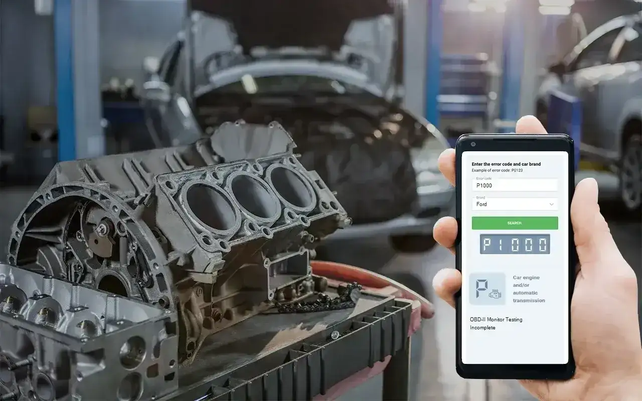 Mechanik sprawdza kod błędu DTC P1000 Ford na telefonie, obok rozebranego silnika w warsztacie.