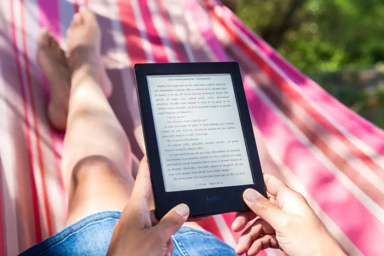 Osoba relaksuje się w hamaku, czytając e-booka. Idealny sposób na wakacje, gdy szukasz najlepszego czytnik ebook ranking.