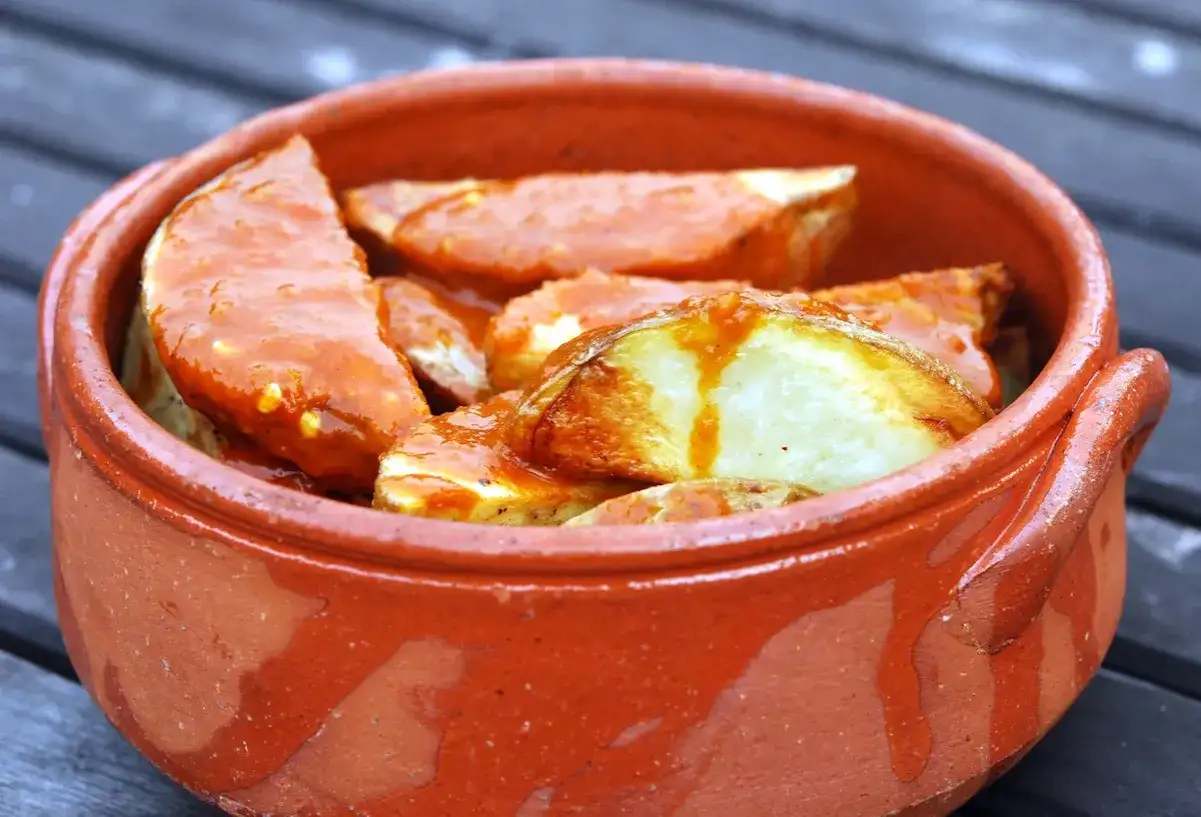 Patatas bravas, pommes de terre croustillantes nappées d'une sauce épicée, servies dans un plat en terre cuite.