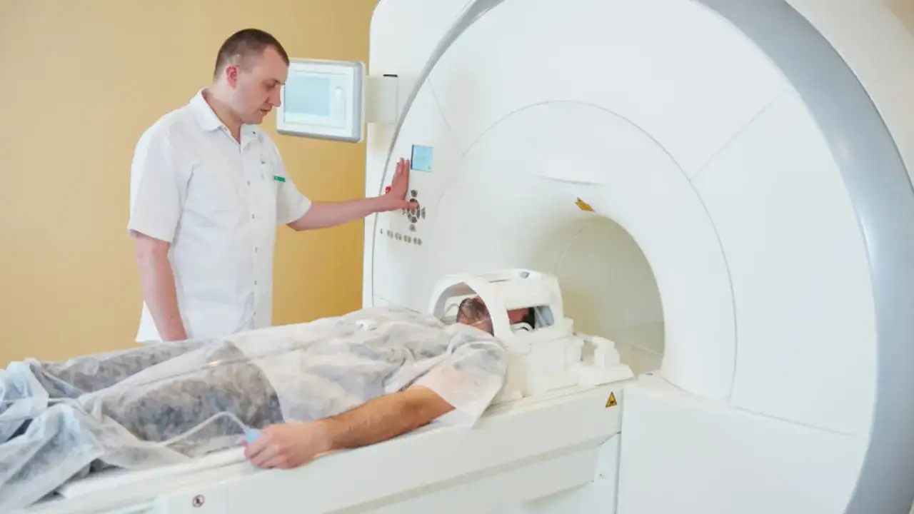 Pacjent leży w aparacie do rezonansu magnetycznego. Technik nadzoruje badanie, przygotowując rejestrację.