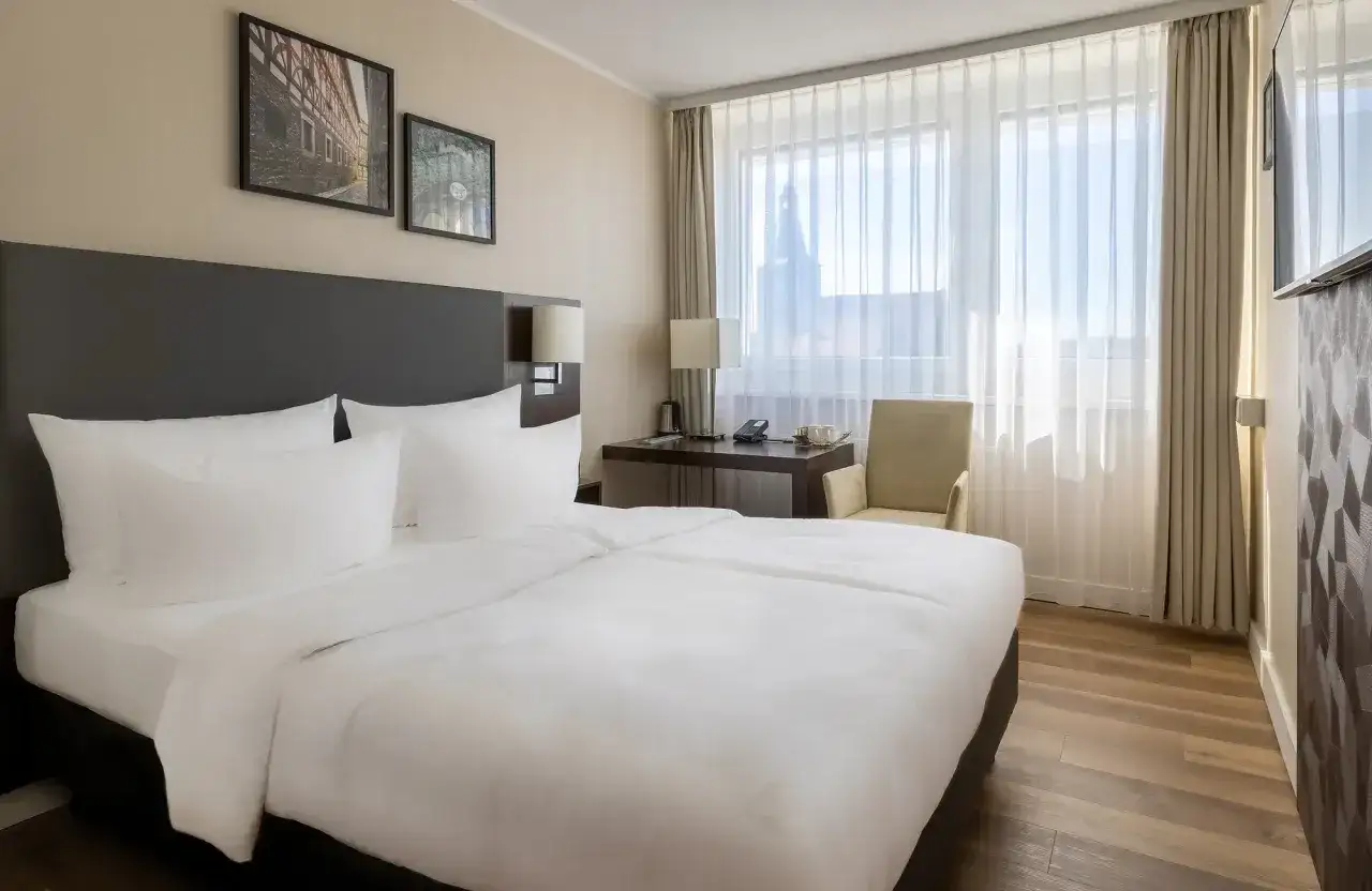 Przytulny pokój w hotelu Radisson Blu Erfurt z białym pościelonym łóżkiem, biurkiem i oknem z widokiem na miasto.