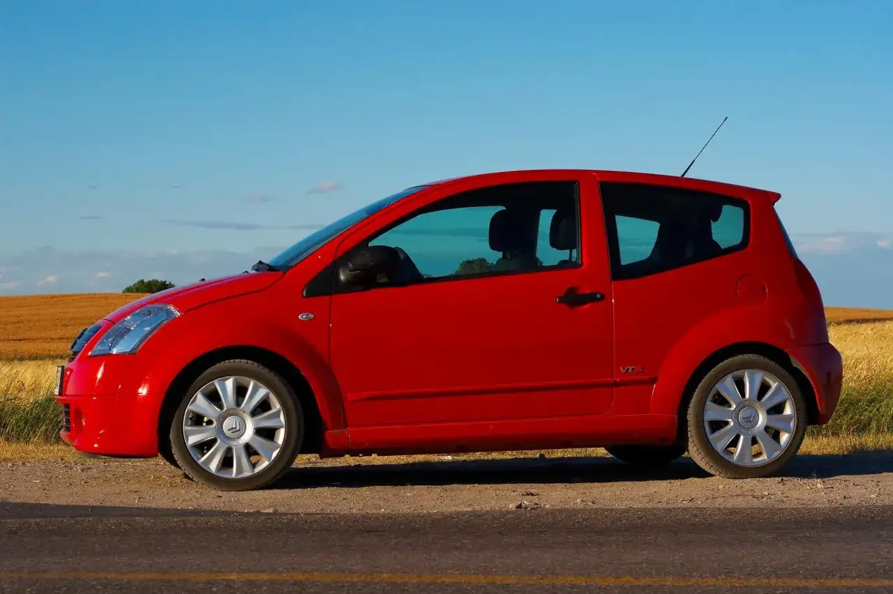 Czerwony Citroen C2 VTR stoi na poboczu drogi, na tle złotego pola i błękitnego nieba.
